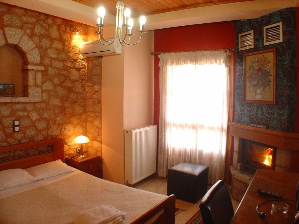 Una habitación de hotel acogedora con una pared de piedra, una chimenea, una cama, una mesita de noche y una ventana con cortinas.