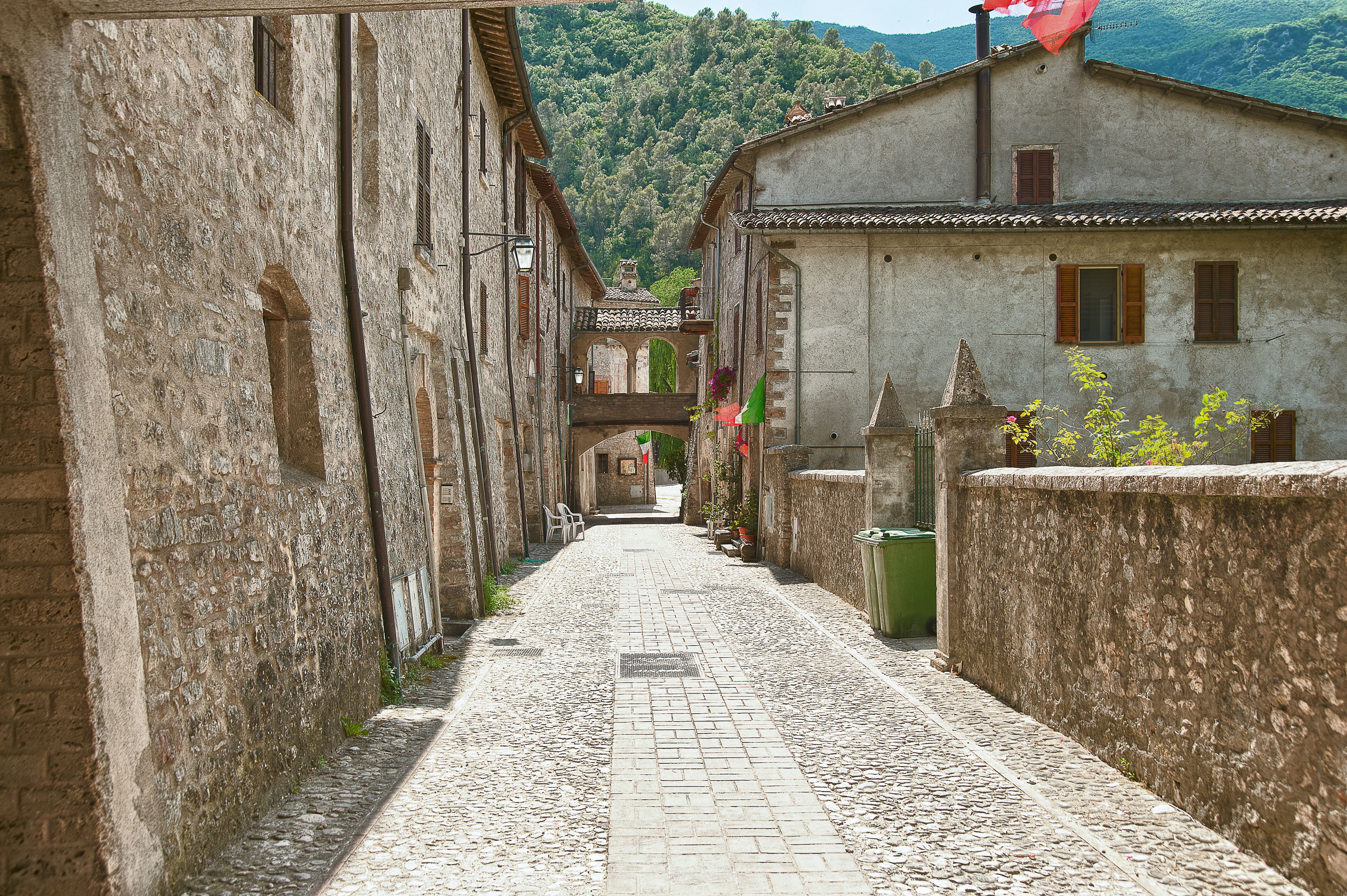 Une ruelle étroite pavée, bordée de bâtiments historiques en pierre, dotés d’entrées en arc de cercle et d’une architecture traditionnelle.