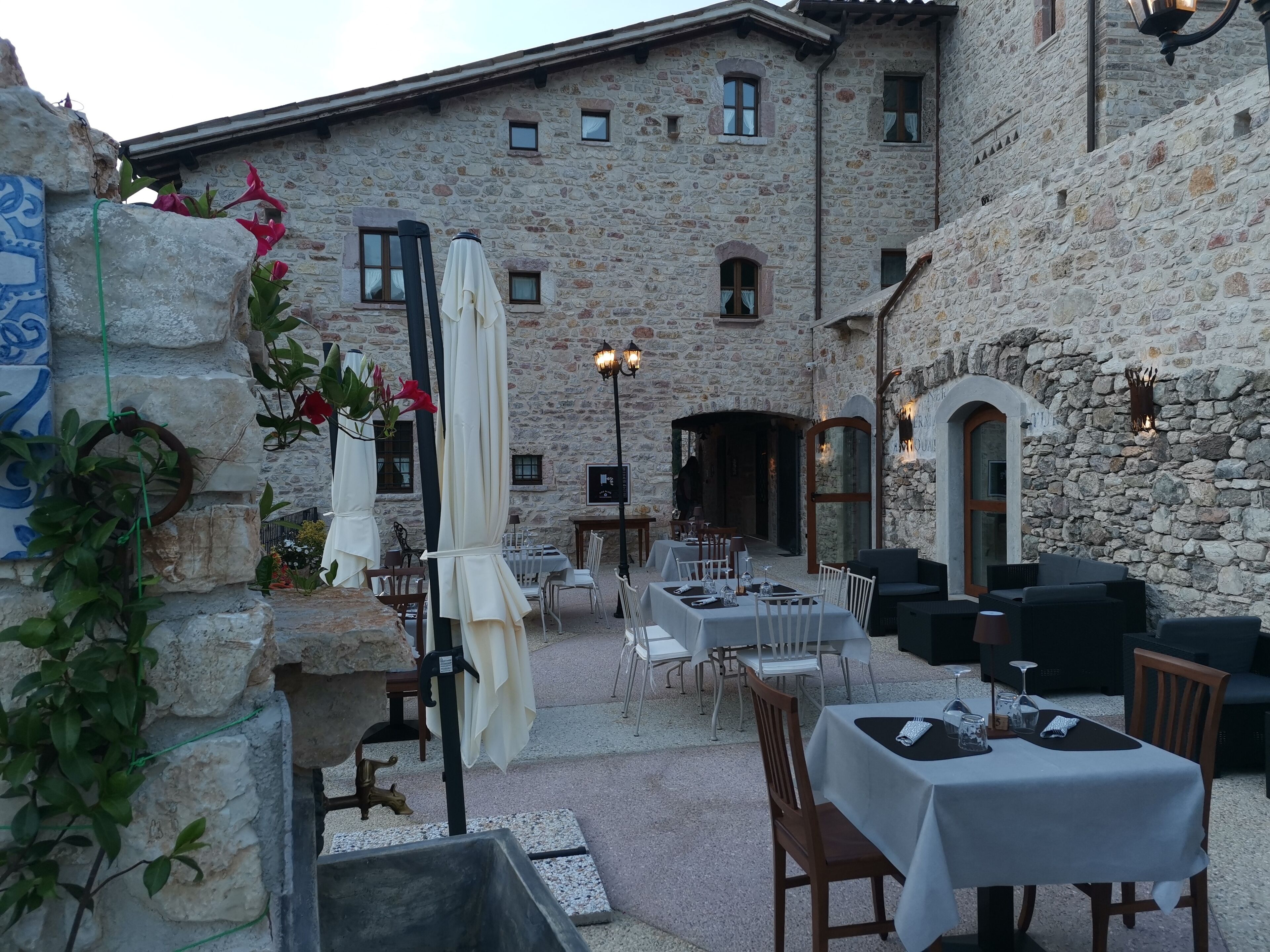 Un área de comedor al aire libre con paredes de piedra, mesas, sillas y sombrillas.