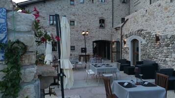 Un área de comedor al aire libre con paredes de piedra, mesas, sillas y sombrillas.
