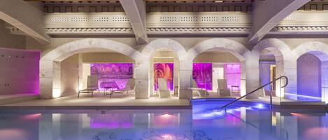 An indoor swimming pool with arched ceilings and a central area with seating and a colorful light display.