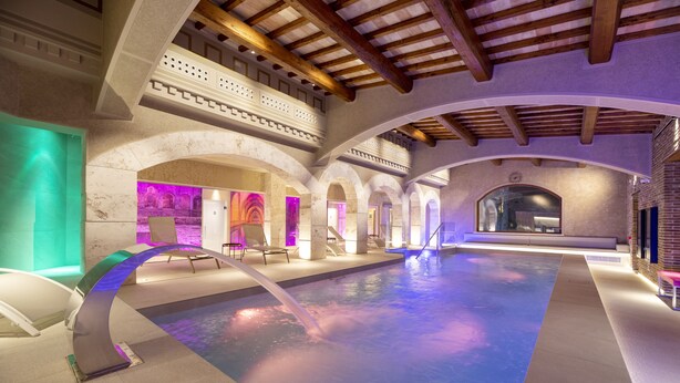 A spacious indoor pool with a modern design, featuring a central water feature and a high ceiling with wooden beams. - Torre Del Nera Albergo Diffuso & Spa (Scheggino)