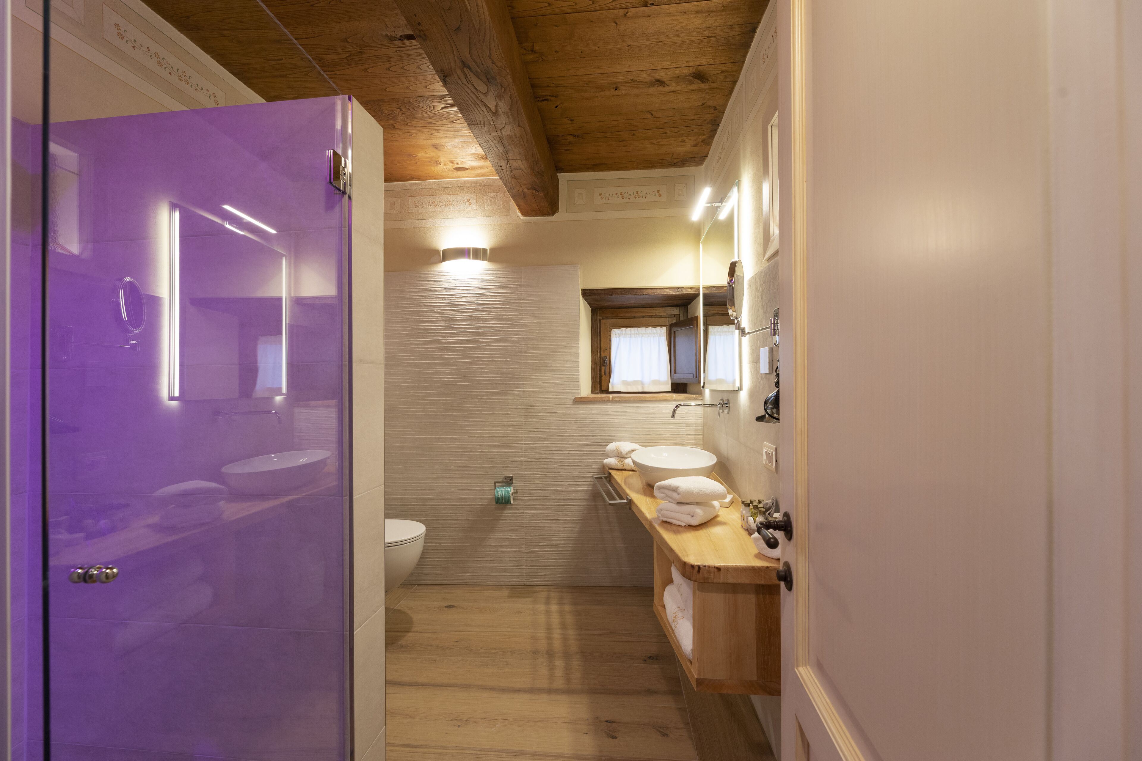 A modern bathroom with a wooden ceiling, a purple door, a white sink, and a mirror above the countertop.