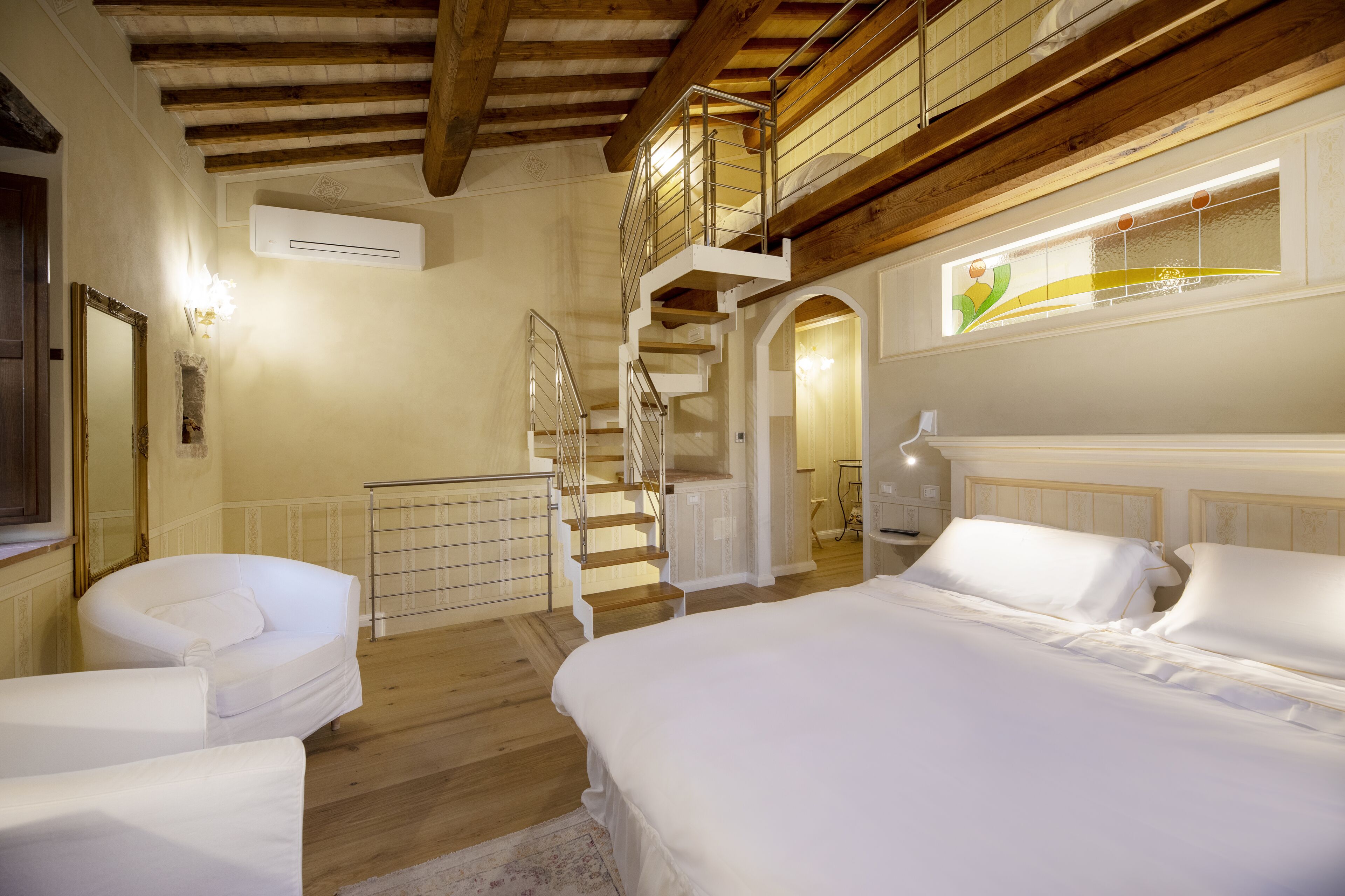 A bedroom with a wooden staircase, a bed, a chair, and a mirror.