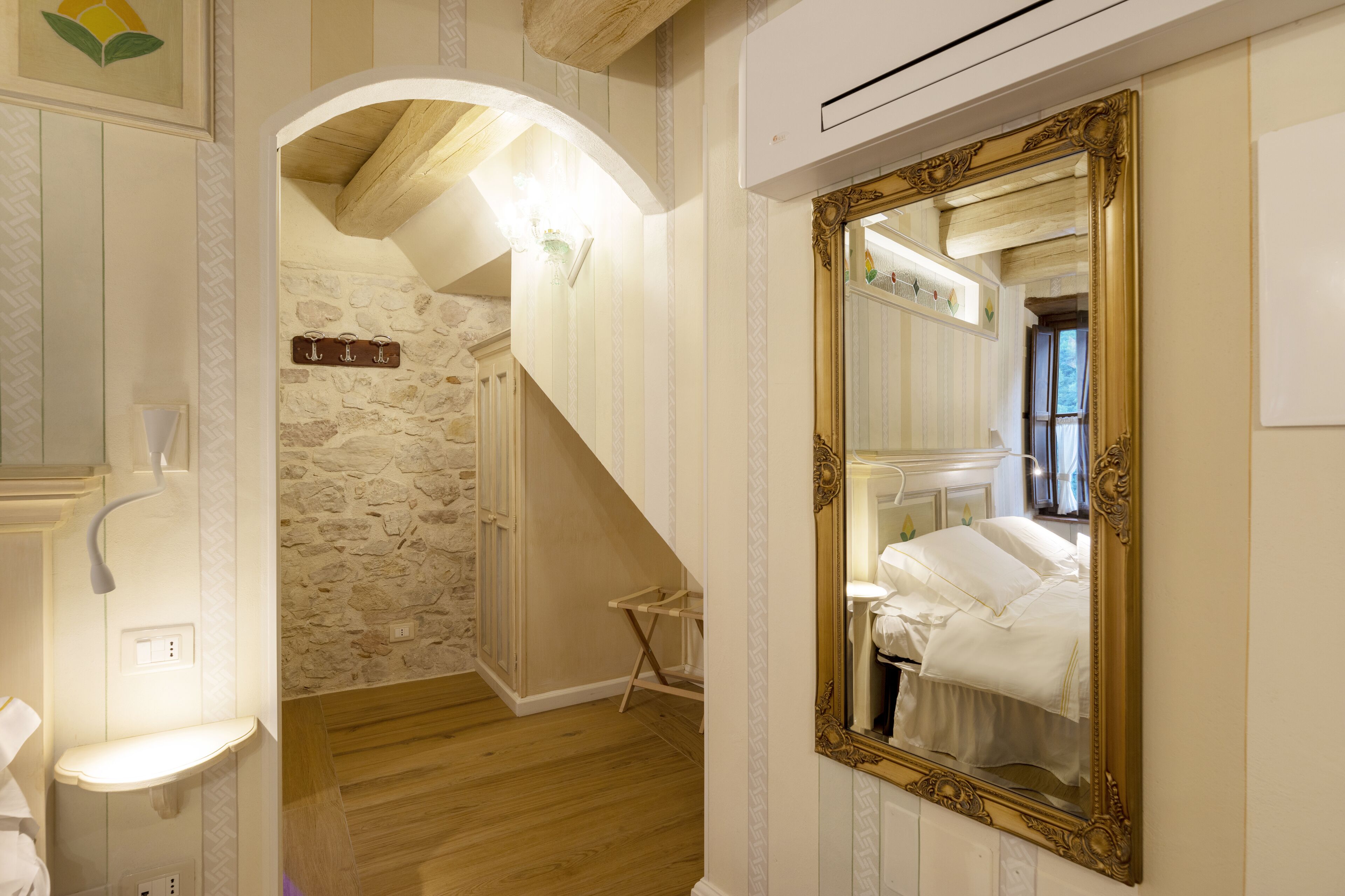 A room with a large ornate mirror, a wooden staircase, and a stone wall.