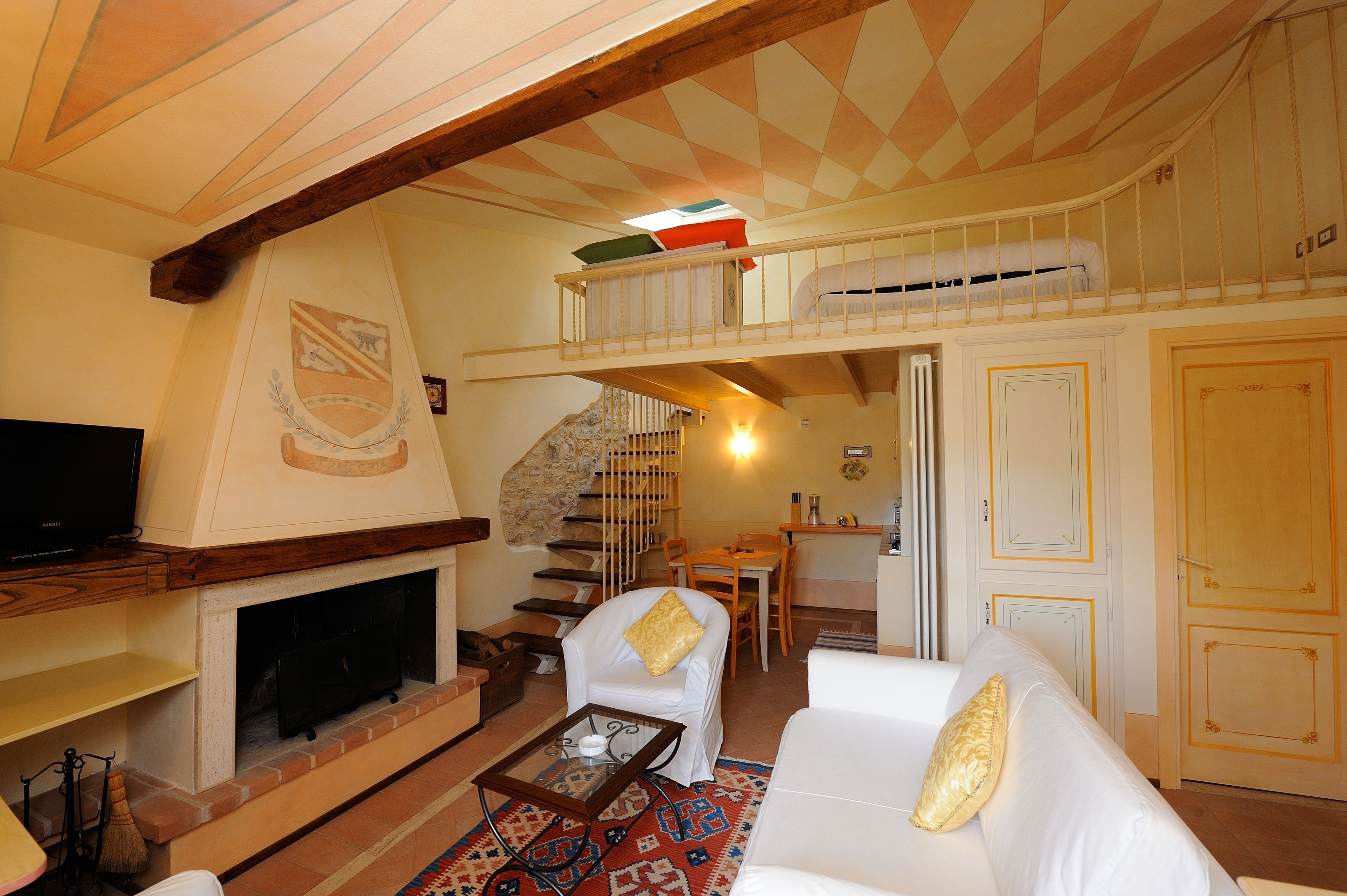 Una sala de estar acogedora con chimenea, un sofá, una mesa de centro y un televisor. Se ve una escalera que sube a una zona superior con una cama.