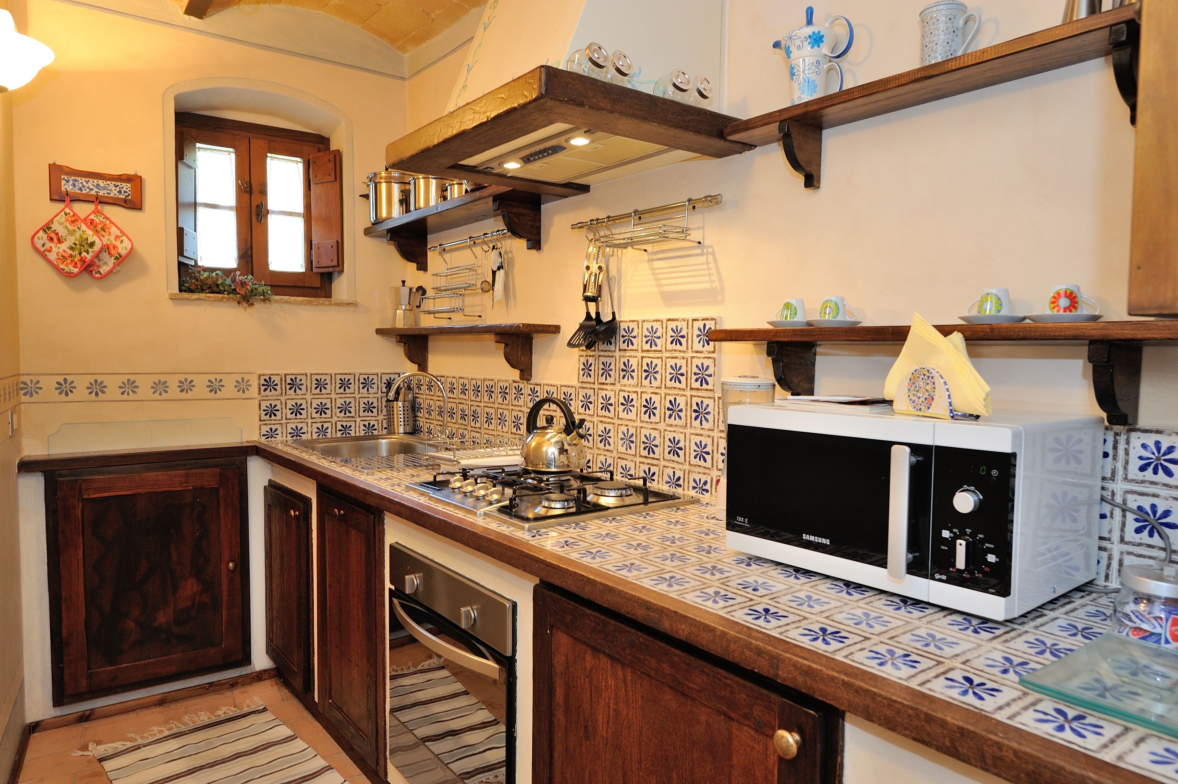 Una cocina con salpicadero de azulejos, armarios de madera, un microondas y una estufa.