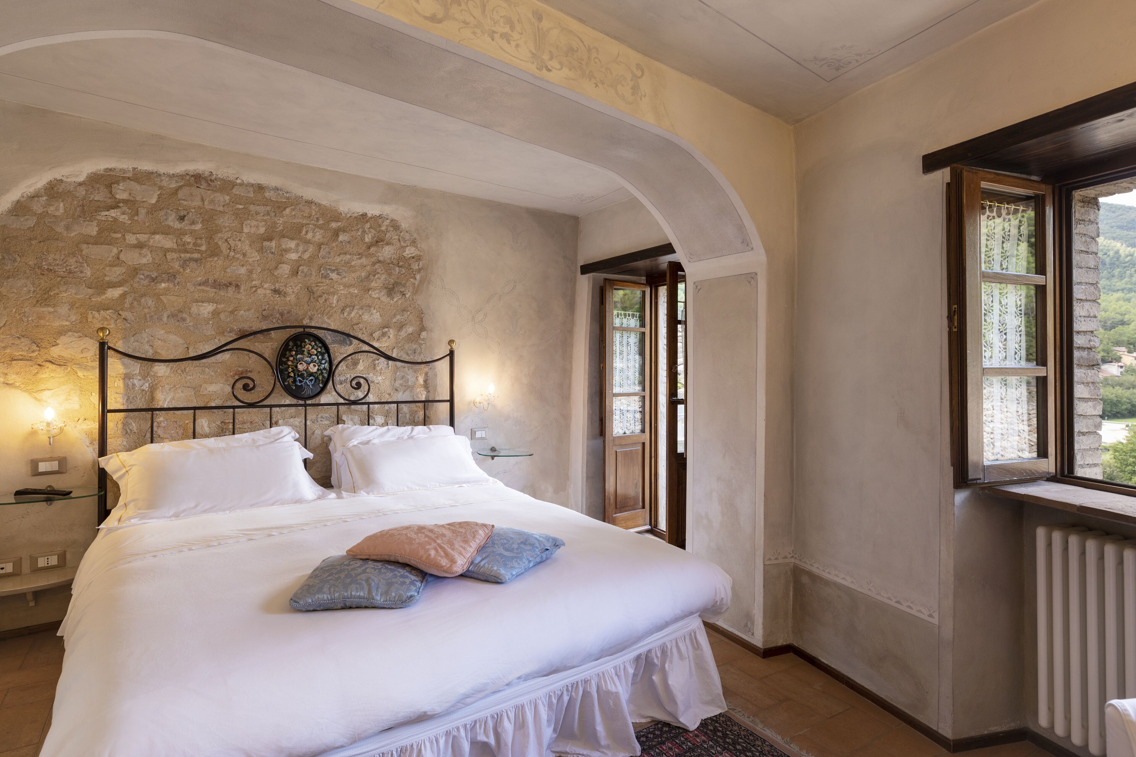 Une chambre avec un mur en pierre, un lit avec une literie blanche et une vue sur un paysage montagneux par la fenêtre.