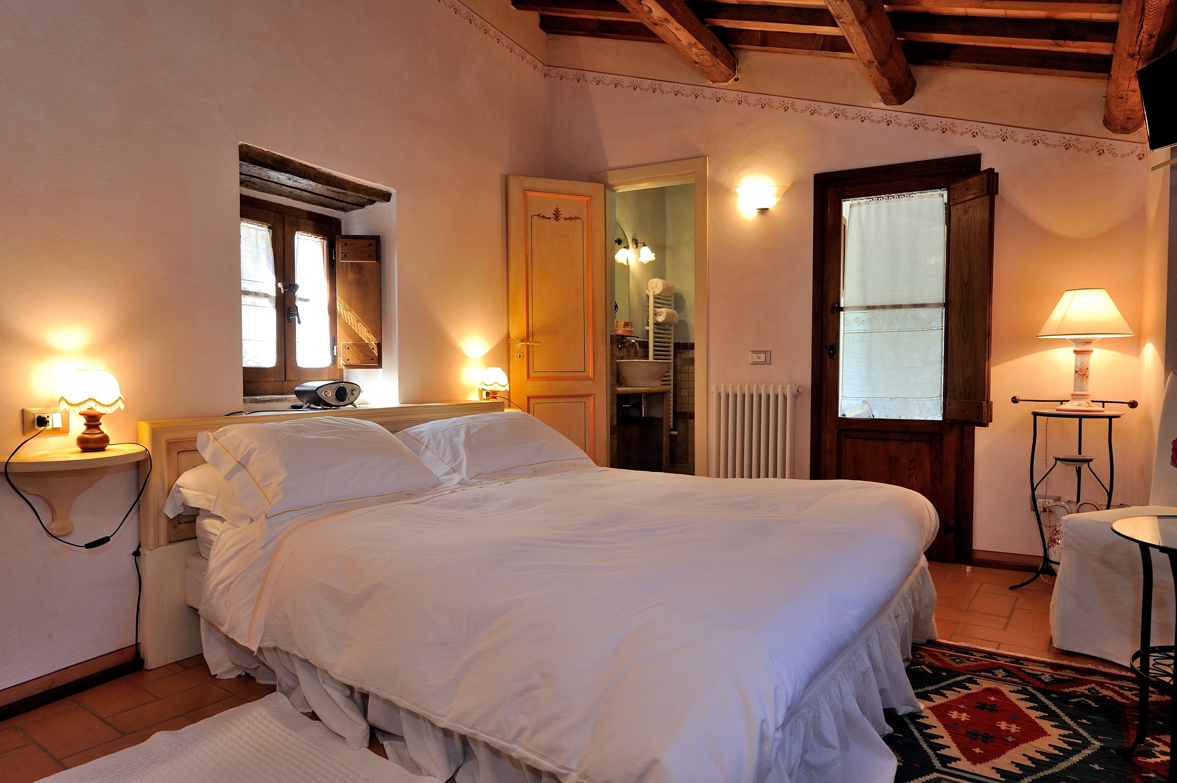 Ein Schlafzimmer mit einem großen Bett, Nachttischlampen, einem Spiegel und einer Holzbalkendecke.