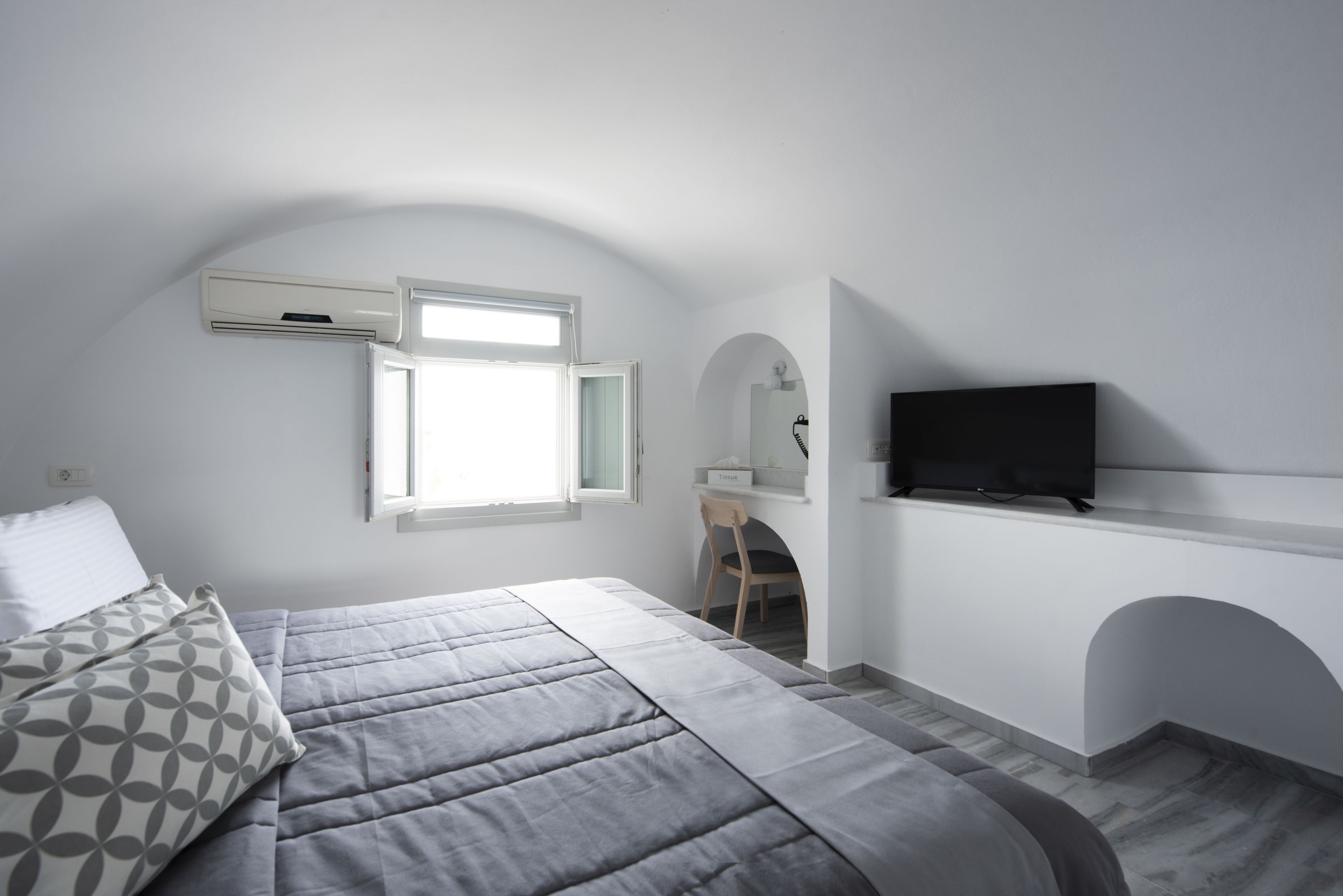 A bedroom with a bed, a TV, a desk, and a window.