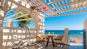 Un espace extérieur aménagé, abrité et doté de sièges, avec vue sur la plage, comprenant des fauteuils en osier, une table avec des boissons et une pergola ornée de fleurs.