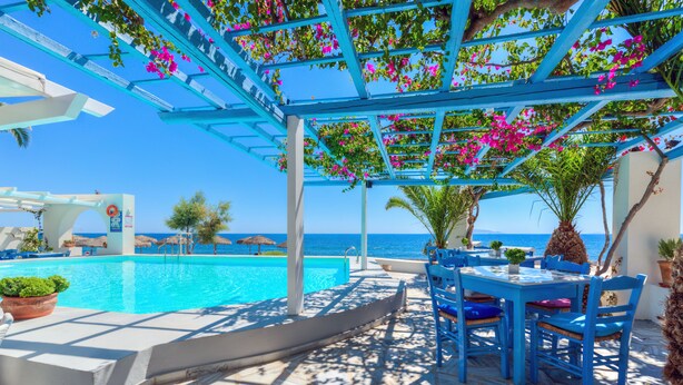 Un espace aménagé au bord de la piscine, avec une pergola recouverte de fleurs roses, une piscine et une vue sur la mer.