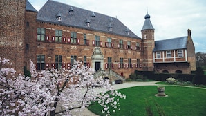 A historic building with a brick facade, a tower, and a well-maintained garden with blooming trees. - Hotel Restaurant Ruimzicht (Zeddam)
