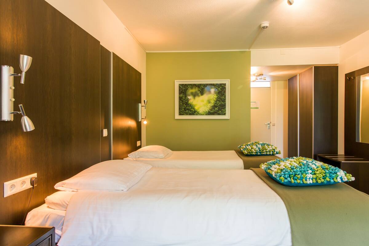 A hotel room with two beds, a green wall, a framed picture, and a mirror.