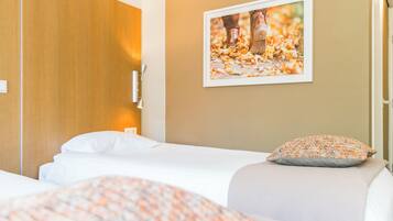 Habitación de hotel con cabecera de madera, un cuadro en la pared y un edredón estampado en la cama.