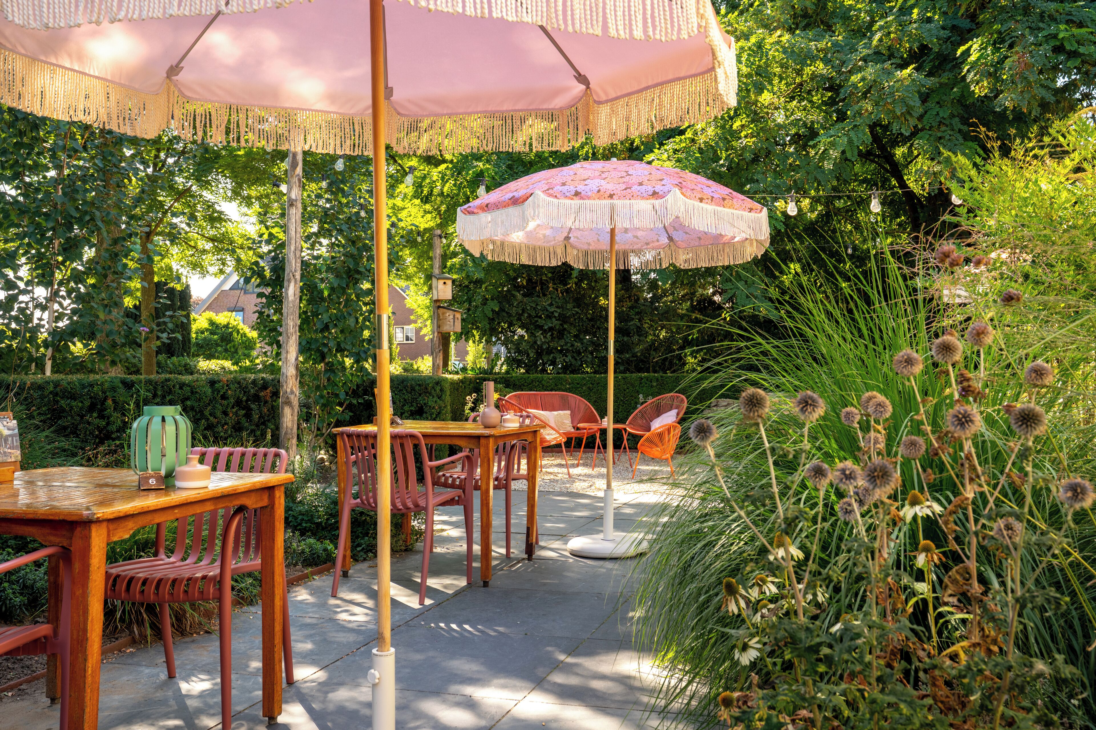 Een terras buiten met houten meubels, een tafel en twee parasols.