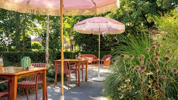 Een terras buiten met houten meubels, een tafel en twee parasols.