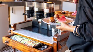 A person serving coffee at a counter with a coffee machine, a tray with pastries, and a coffee grinder. - Hotel Restaurant Ruimzicht (Zeddam)