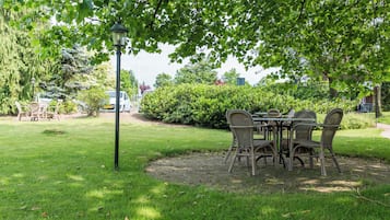 A garden with a table and chairs under a tree, surrounded by greenery.