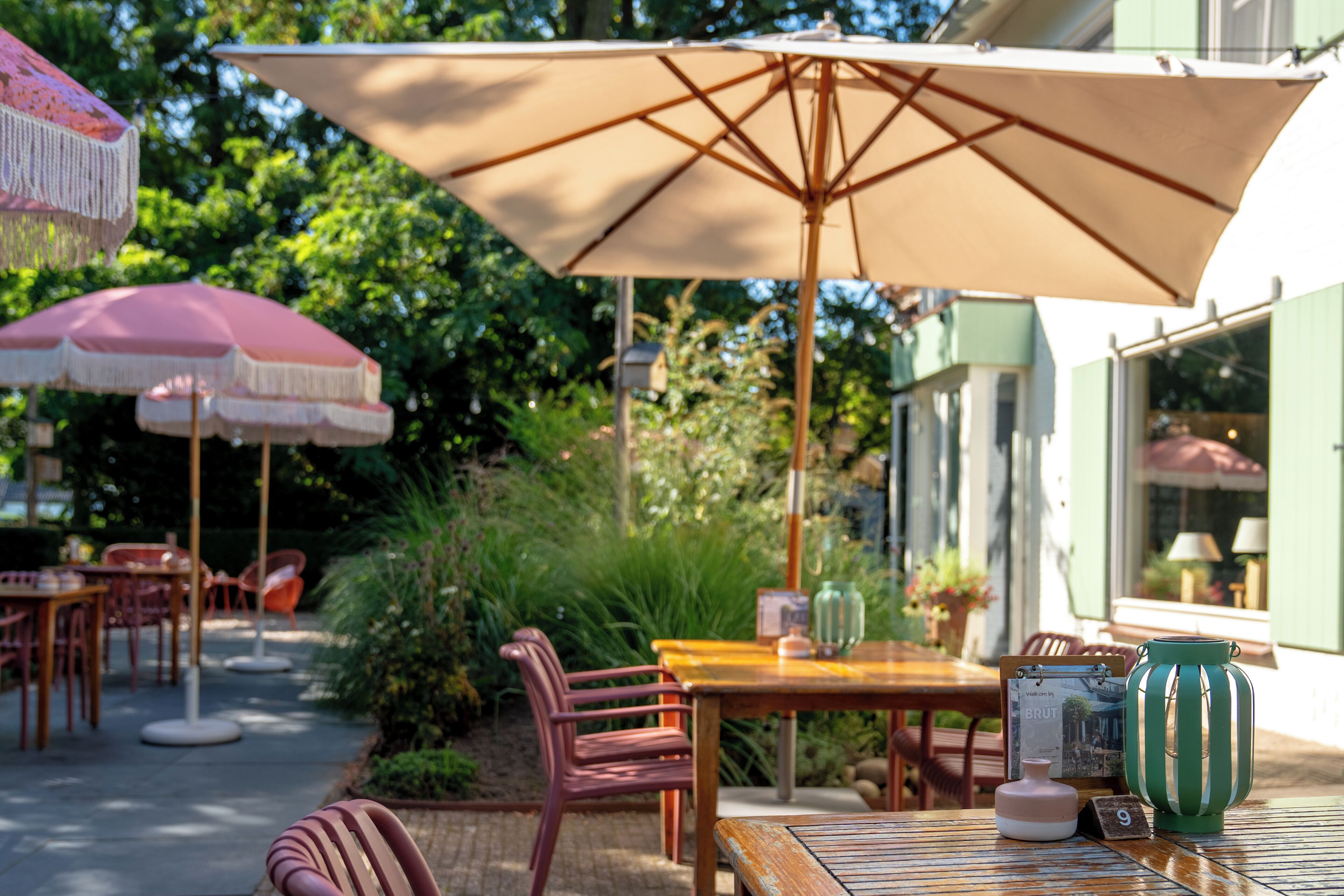 An outdoor patio with tables and chairs, a large umbrella, and a green-striped vase.