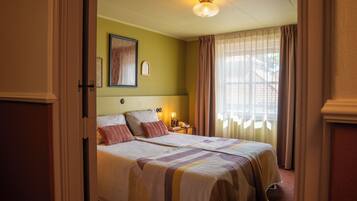 A hotel room with a large bed, a nightstand, a lamp, and a window with curtains.