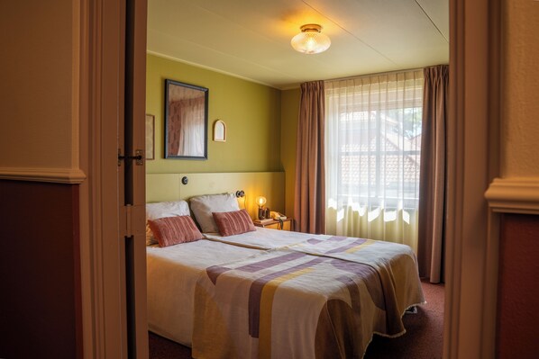 Una habitación de hotel con una cama grande, una mesita de noche, una lámpara y una ventana con cortinas.