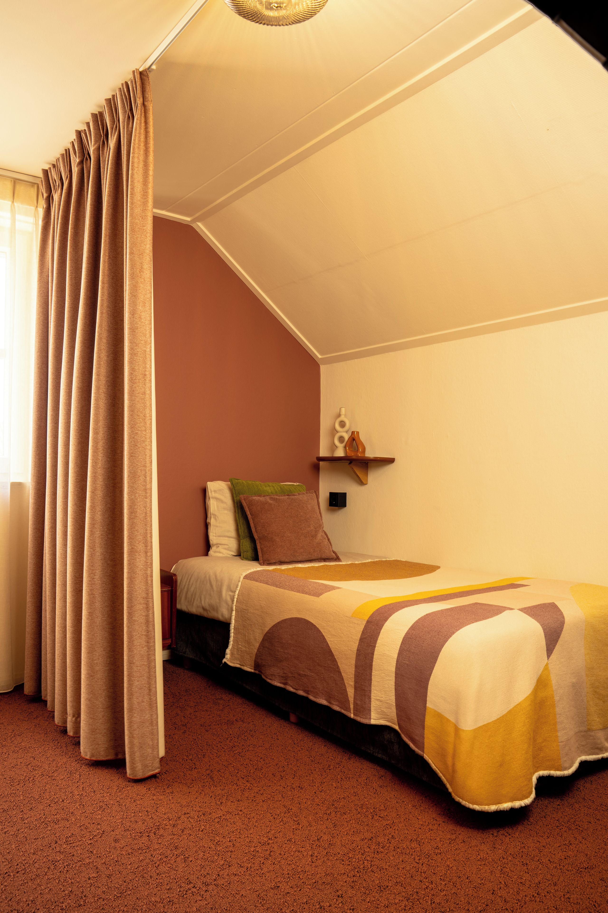 Una camera da letto con un letto singolo, un comodino, una mensola a muro e una finestra con tende.