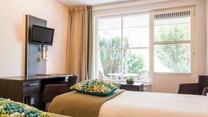 A hotel room with a bed, a desk with a TV, a window with a view of trees, and a chair. - Hotel Restaurant Ruimzicht (Zeddam)