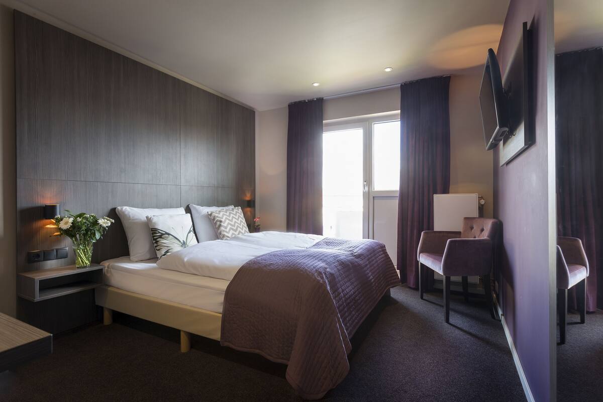 A modern hotel room with a large bed, bedside tables, a desk, and a chair.