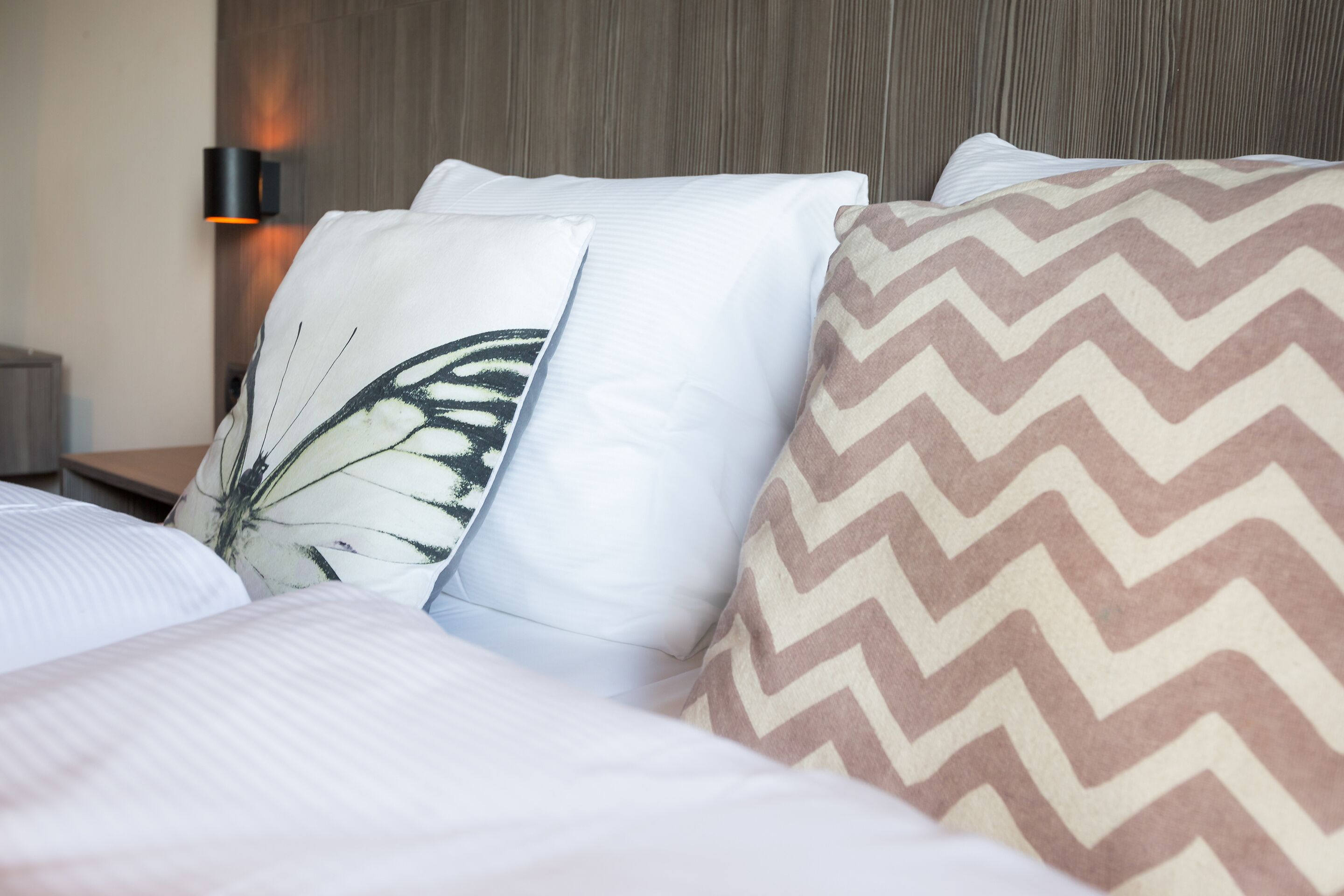 Una cama bien hecha con almohadillas estampadas y una lámpara fijada a la pared.