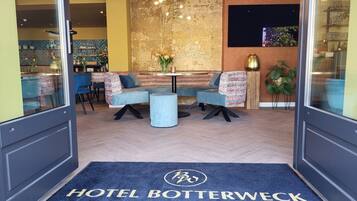 A hotel lobby with a modern design, featuring a seating area with sofas and a table, a decorative wall, and a welcome mat with the hotel's name.