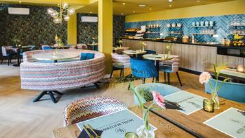 Un restaurante con mesas redondas, asientos estampados y una zona de bar con estanterías llenas de vajilla y copas.