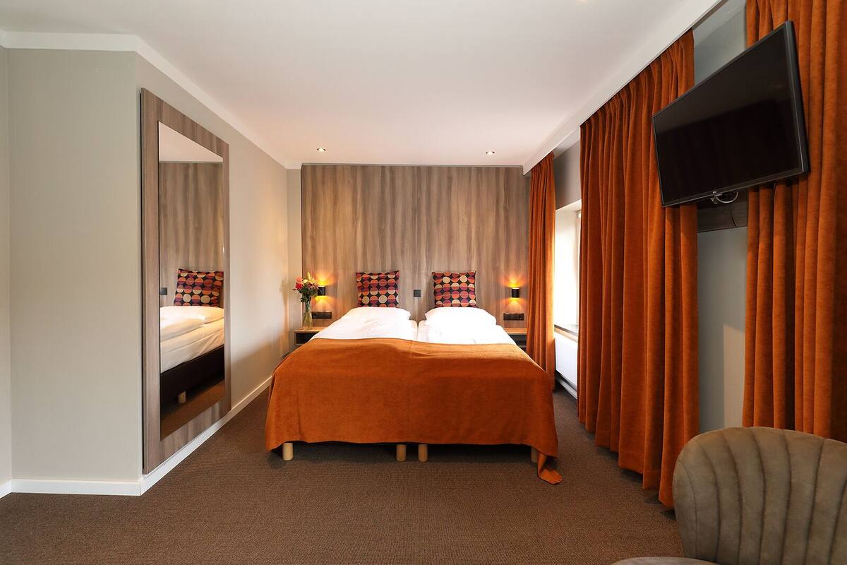 A hotel room with a double bed, a TV mounted on the wall, and a mirror on one side.