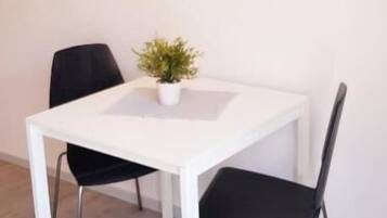 A white dining table with two black chairs, a potted plant, and a wall-mounted light fixture.