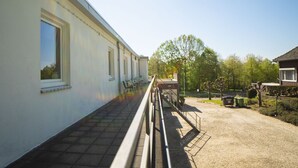 Un bâtiment doté d’un long couloir rectiligne et d’un petit espace jardin avec un banc et une poubelle.