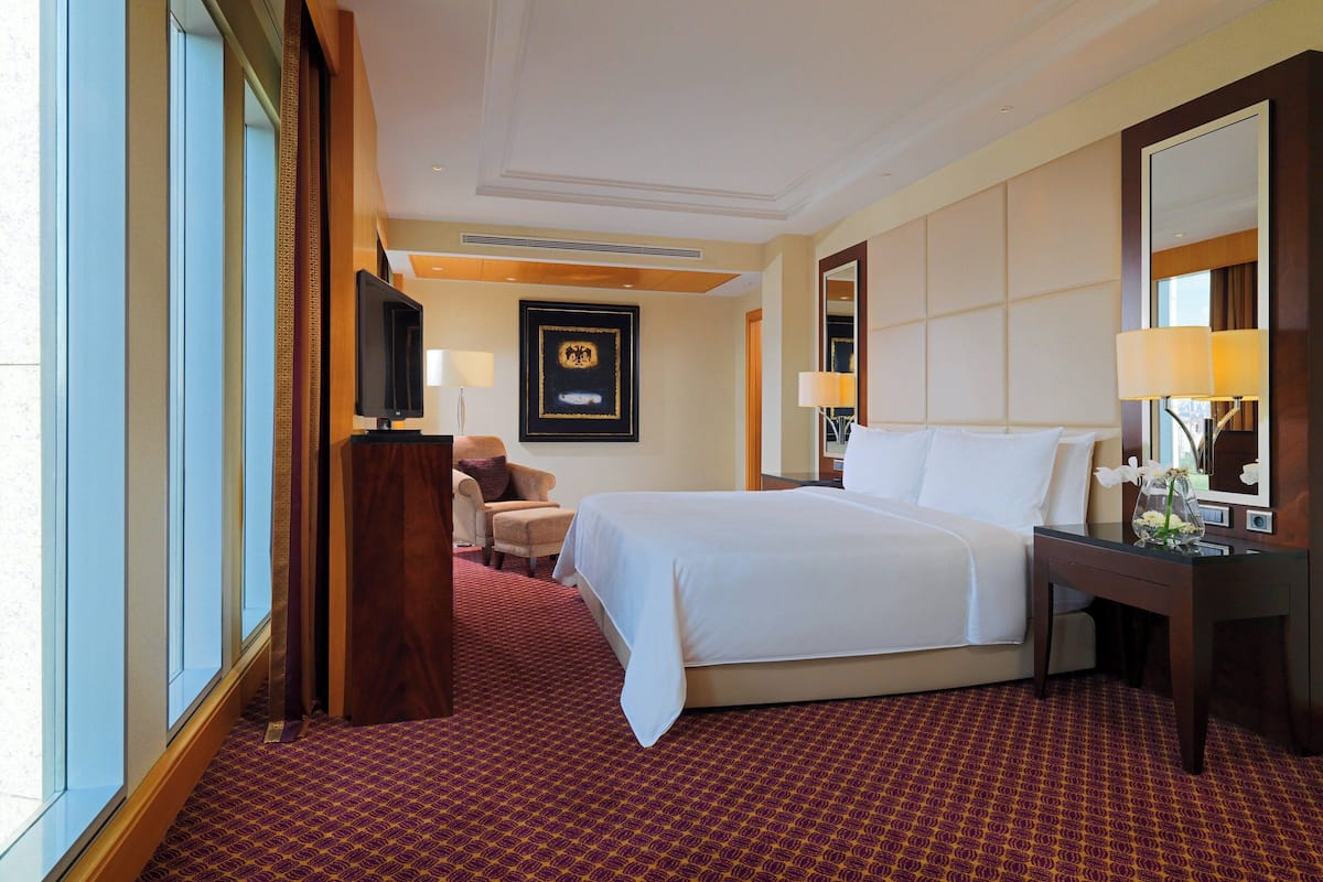 A hotel room with a large bed, a desk with a lamp, a chair, a television, and a framed picture on the wall.