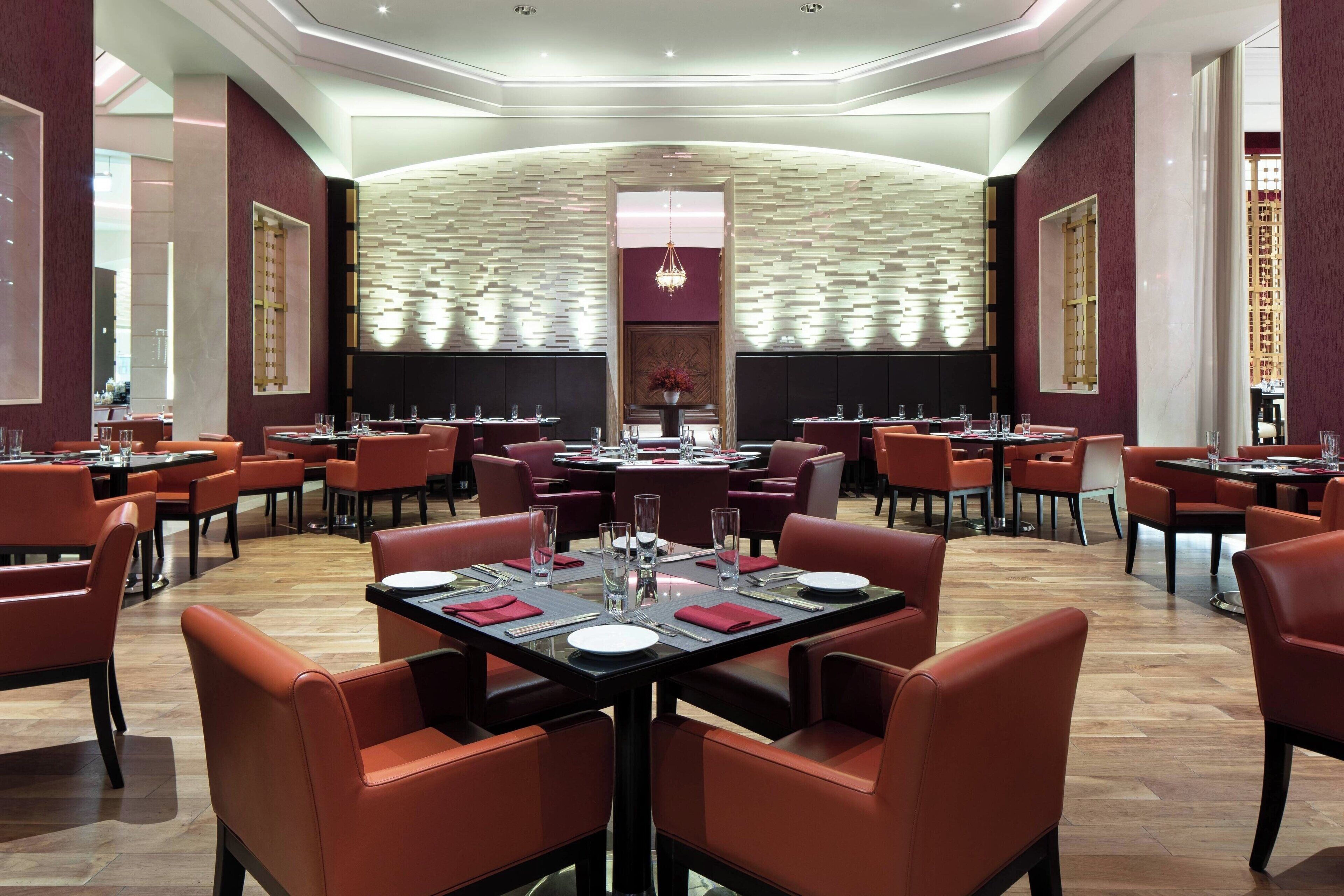 A spacious restaurant with multiple tables and chairs, a central decorative wall, and a chandelier.