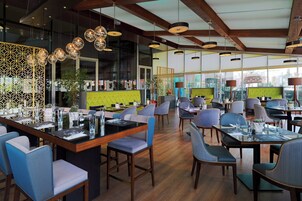 A modern restaurant with a bar area, wooden ceiling beams, and a variety of seating options including bar stools and chairs.