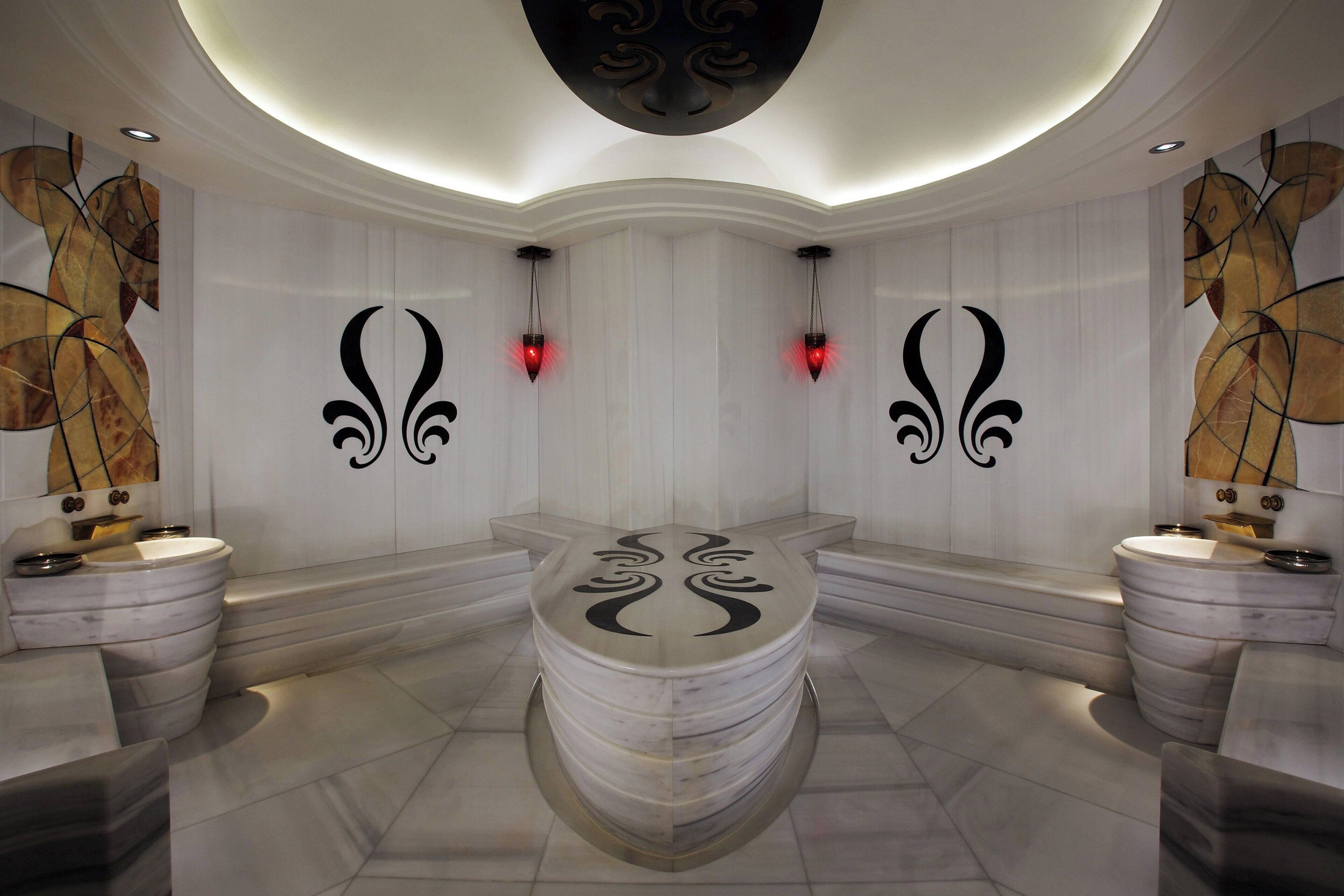 Une salle de bain moderne avec un lavabo central en marbre, deux appliques murales et des œuvres d’art abstraites accrochées au mur.