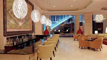 Un vestíbulo de hotel con zona de bar, asientos y una escalera.