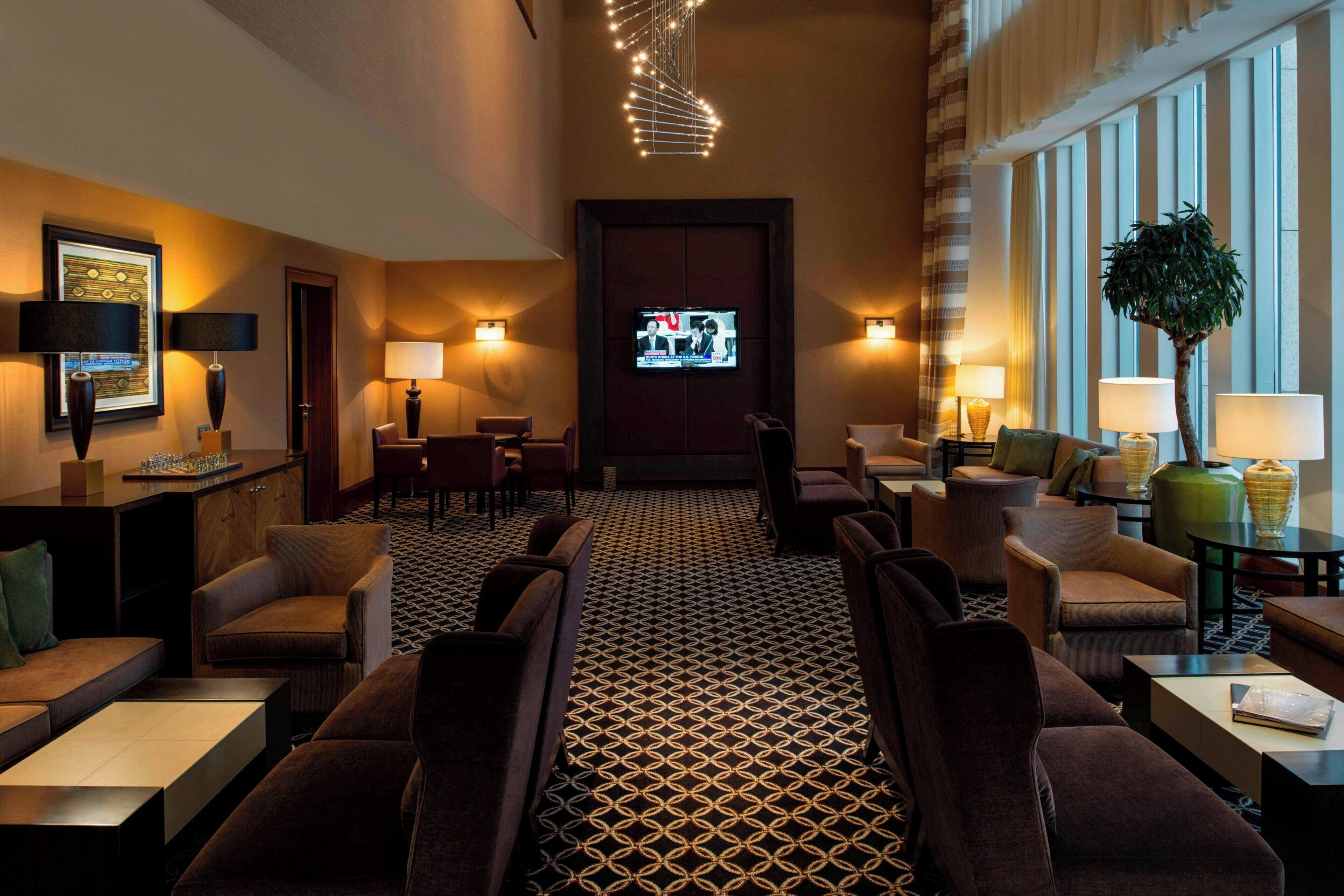 Un vestíbulo de hotel con piso estampado, zonas de estar, lámparas fijadas a la pared y una pantalla de televisión.