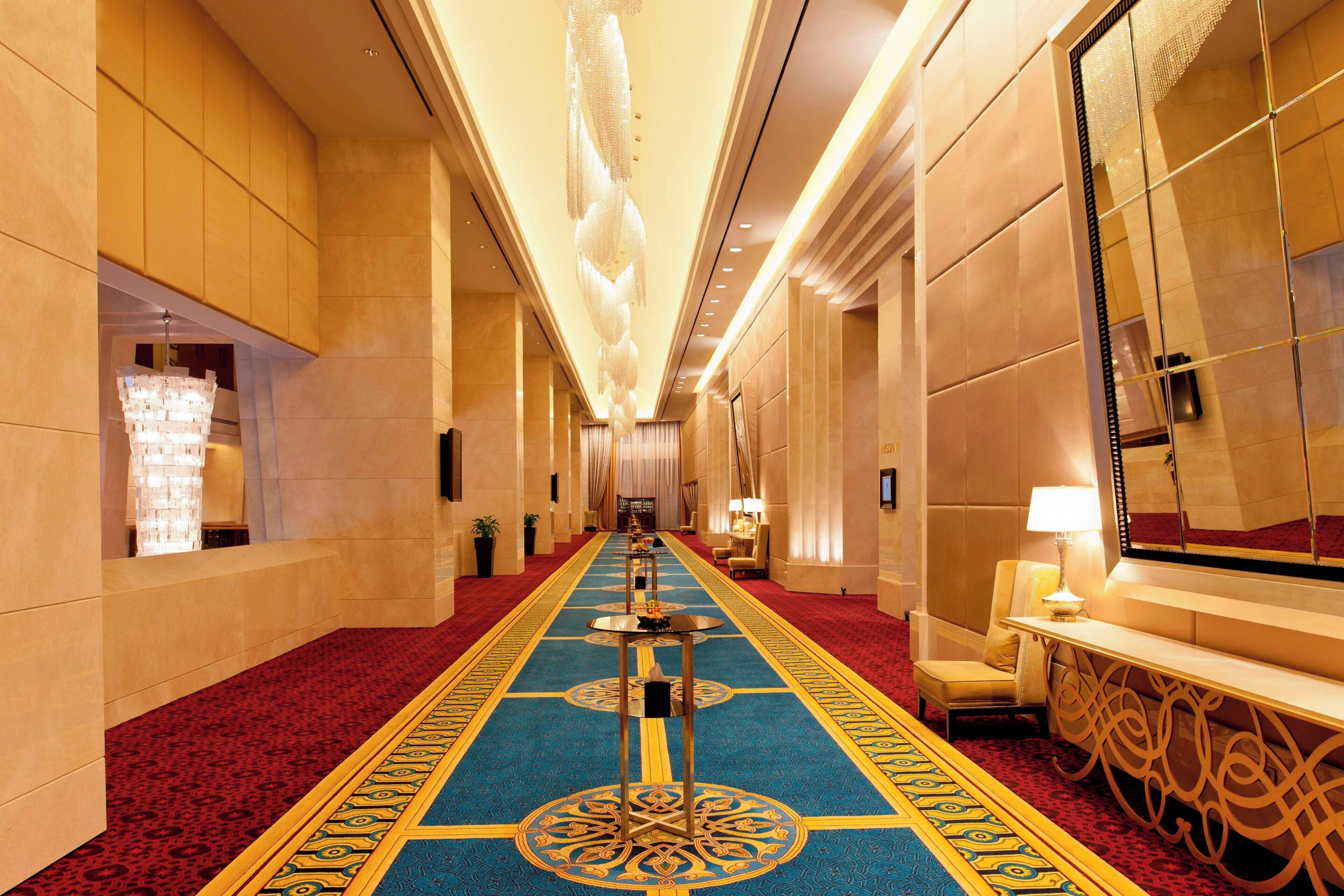 Pasillo de hotel con alfombra roja, suelo estampado y una columna central.