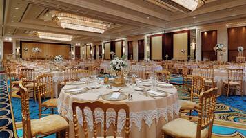 A banquet hall with round tables, gold chairs, and chandeliers.
