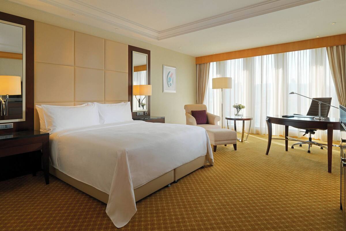 A hotel room with a large bed, a desk, a chair, and a small table.