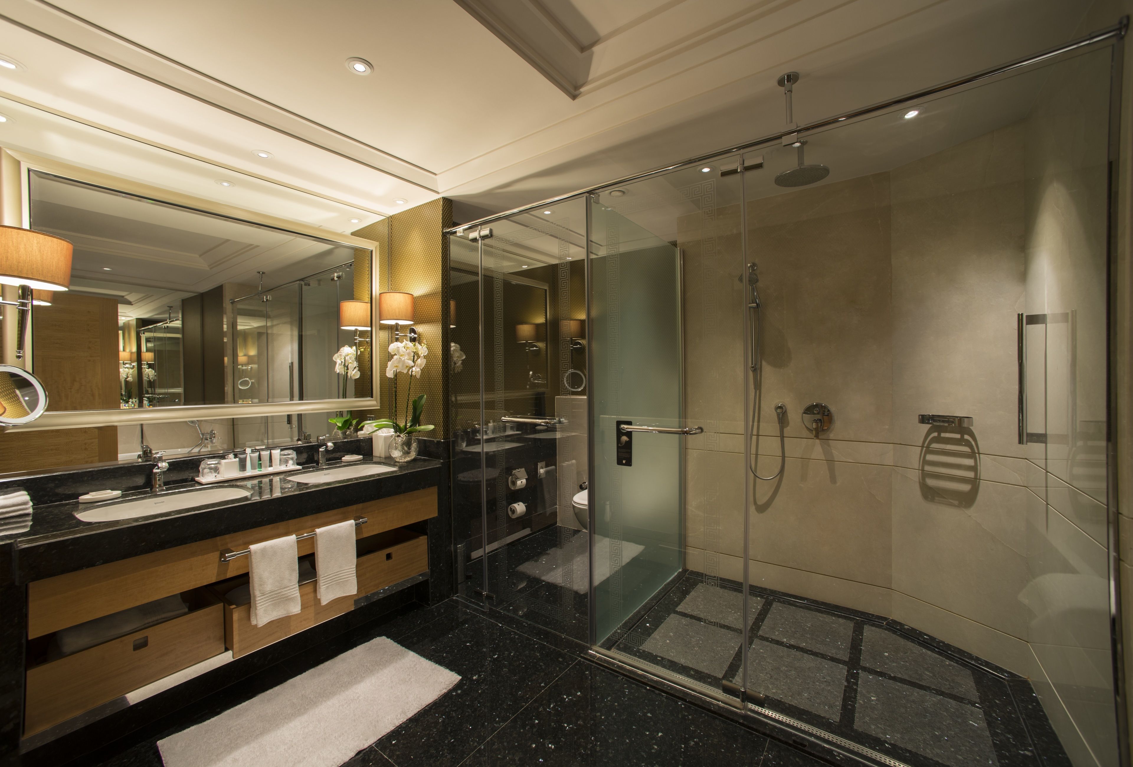 Un baño moderno con ducha envuelta en vidrio, tocador con doble lavabo y un espejo grande.