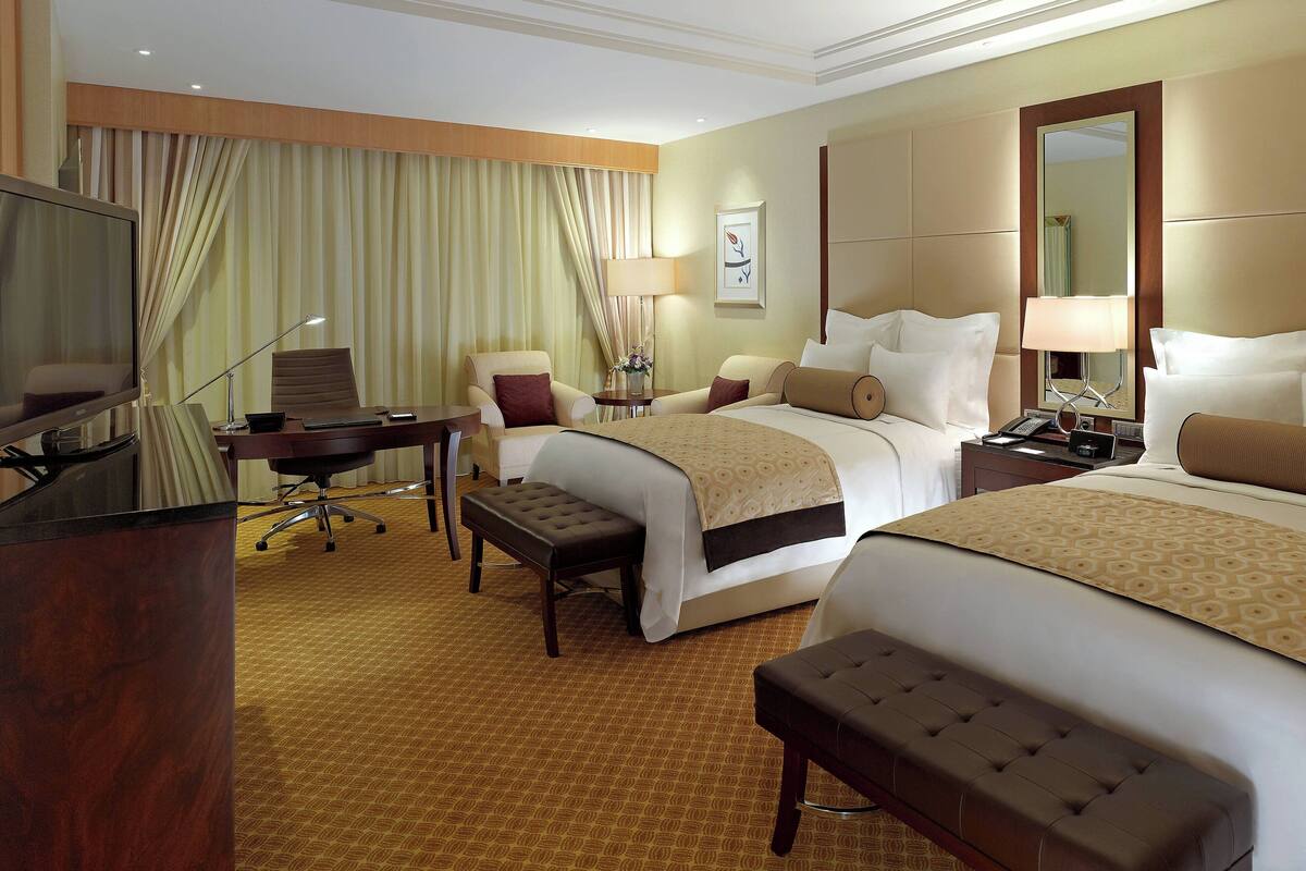 A hotel room with two beds, a desk, a chair, a TV, and a large mirror.