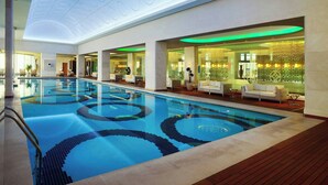 Una piscina interior con diseño de agua cristalina, rodeada de zonas de estar con asientos y una pared decorativa.