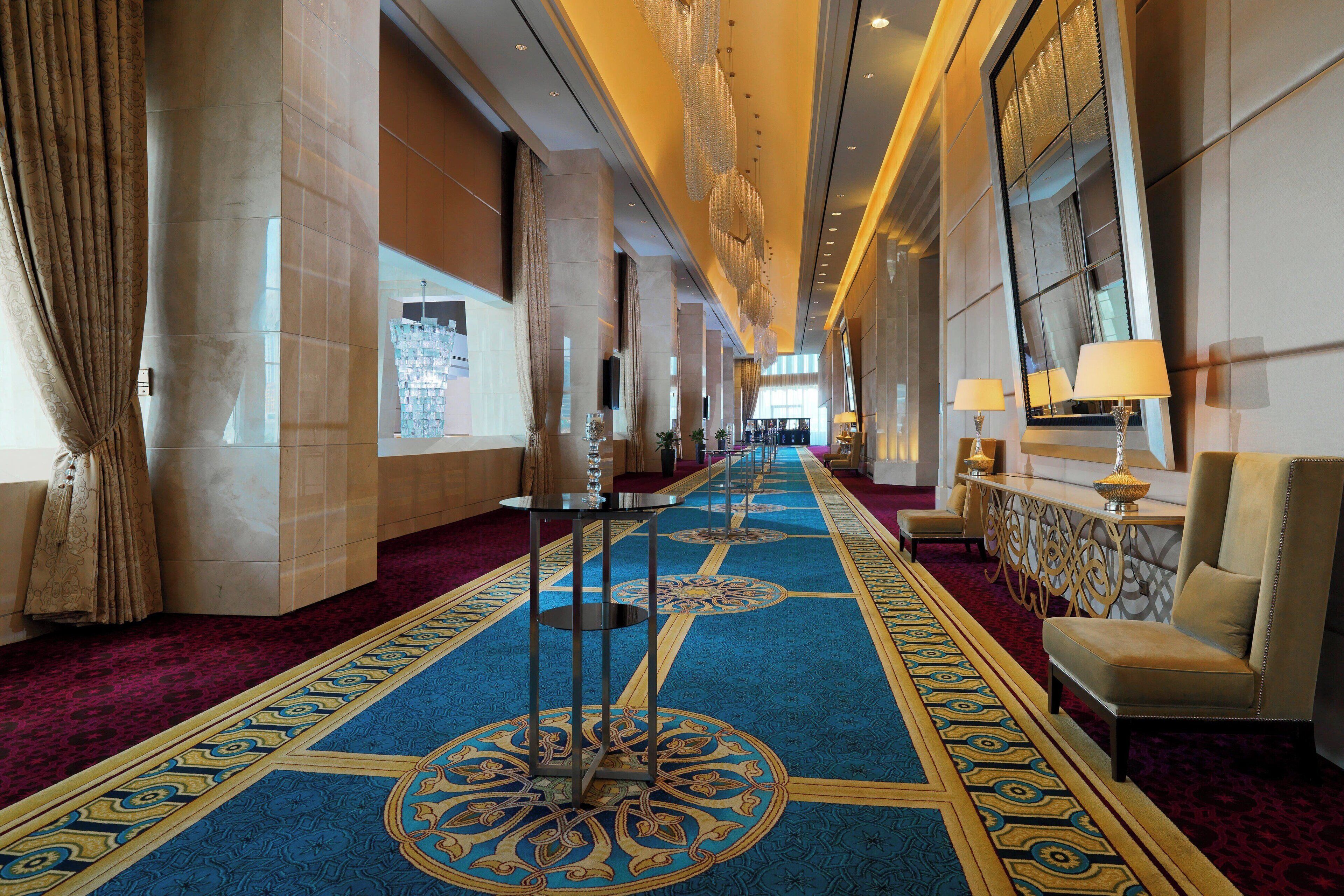 A hotel corridor with a patterned carpet, large columns, and a seating area with a lamp.