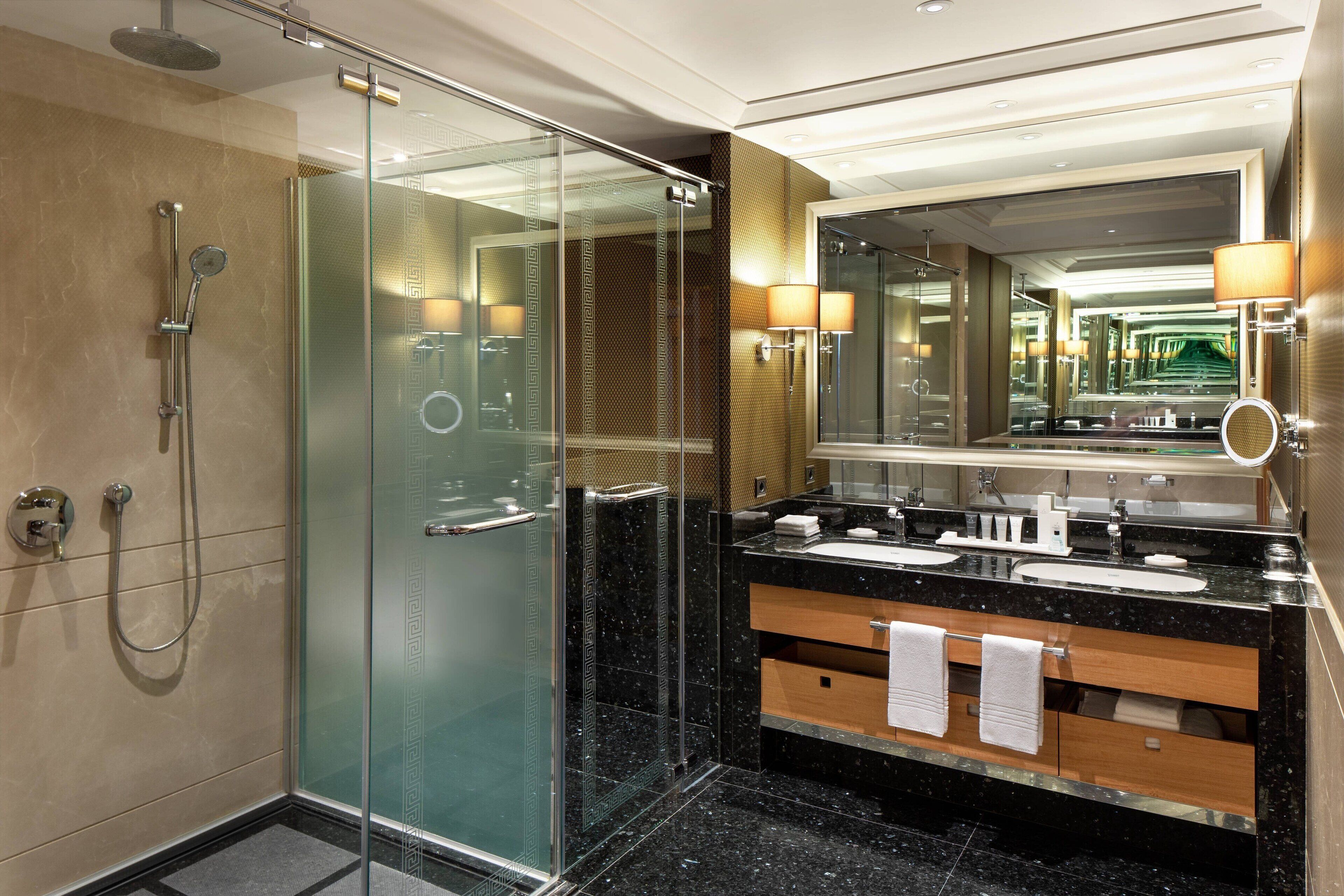 A modern bathroom with a glass-enclosed shower, a black marble vanity with a mirror, and a wooden cabinet.