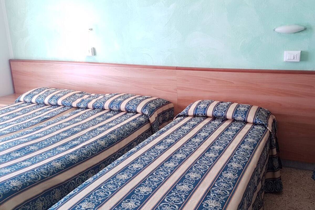 Two beds with striped bedding, a wooden headboard, and a light green wall.